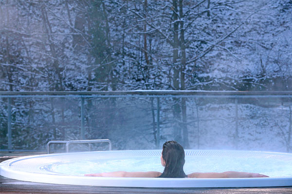 Une femme est dans un jaccuzi sur la terrasse de aquensis à bagnères-de-bigorre. C'est l'hiver, il y a de la neige.