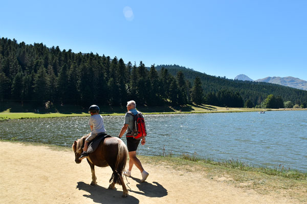 Un enfant et son grand-père font une balade à poney autour du lac de Payolle.